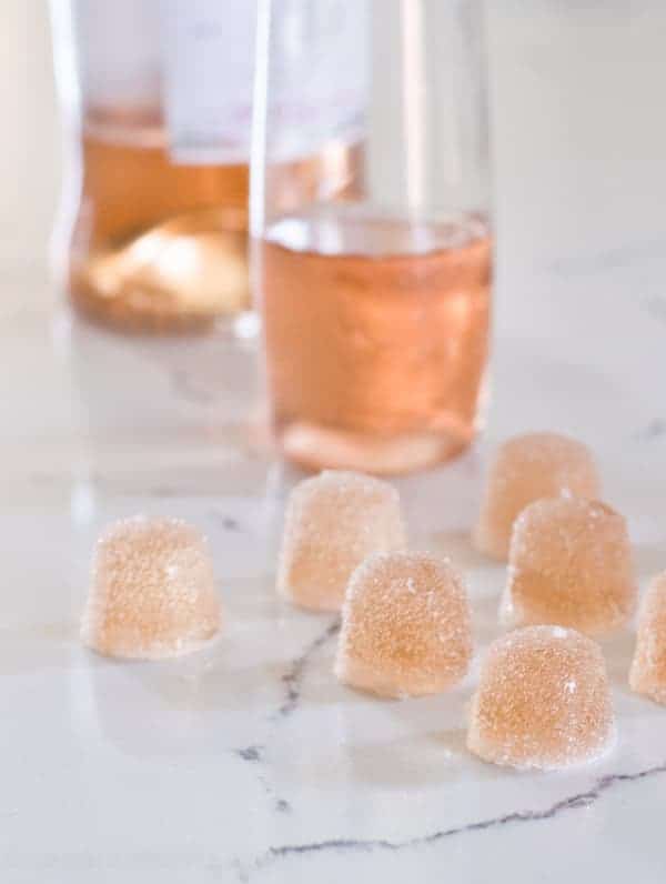 Sugared rosé wine gummies lined up on a white counter with pink wine in the background 