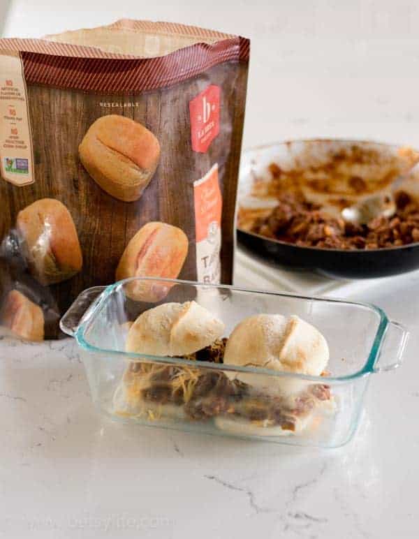 two sloppy joe sliders in a dish next to a bag of frozen dinner rolls