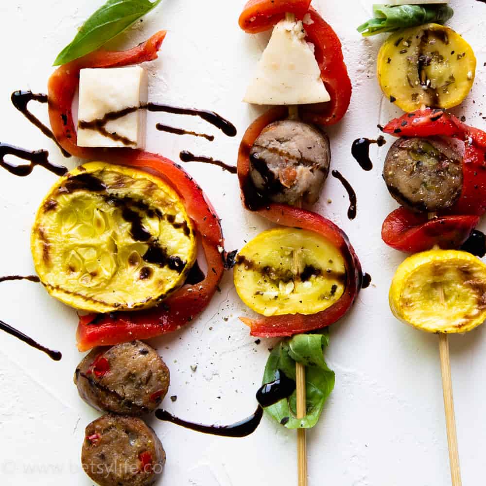 close up detail of sausage slices, cheese cubes, roasted red peppers, and summer squash on a skewer