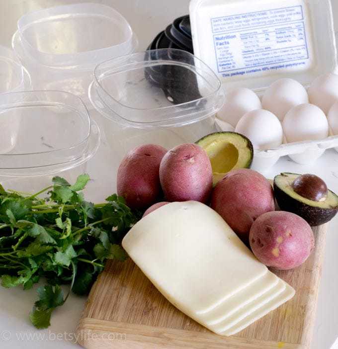 make ahead Breakfast Bowls ingredients on a cutting board. Potatoes, eggs, sliced cheese, avocado, herbs