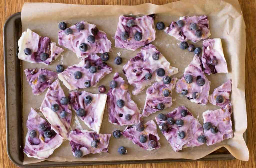 cookie sheet with broken pieces of frozen yogurt bark and blueberries