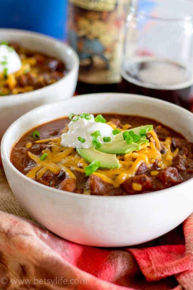 Spicy Beef Beer Chili in a white bowl topped with avocado, sour cream and cheese