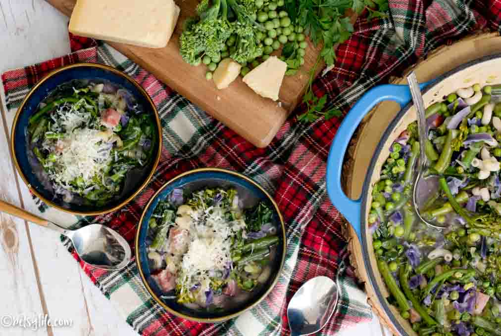 two bowls of healthy minestrone soup next to a large pot of soup on a plaid linen 