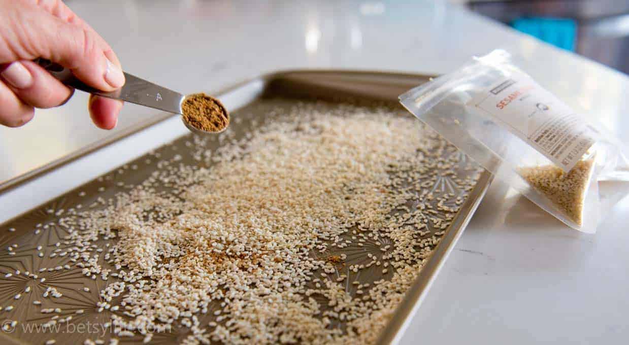 Seasoning sprinkling onto a baking sheet covered in white sesame seeds 