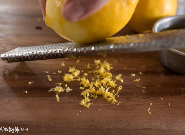 Close up of a lemon being zested on a microplane onto a wooden board