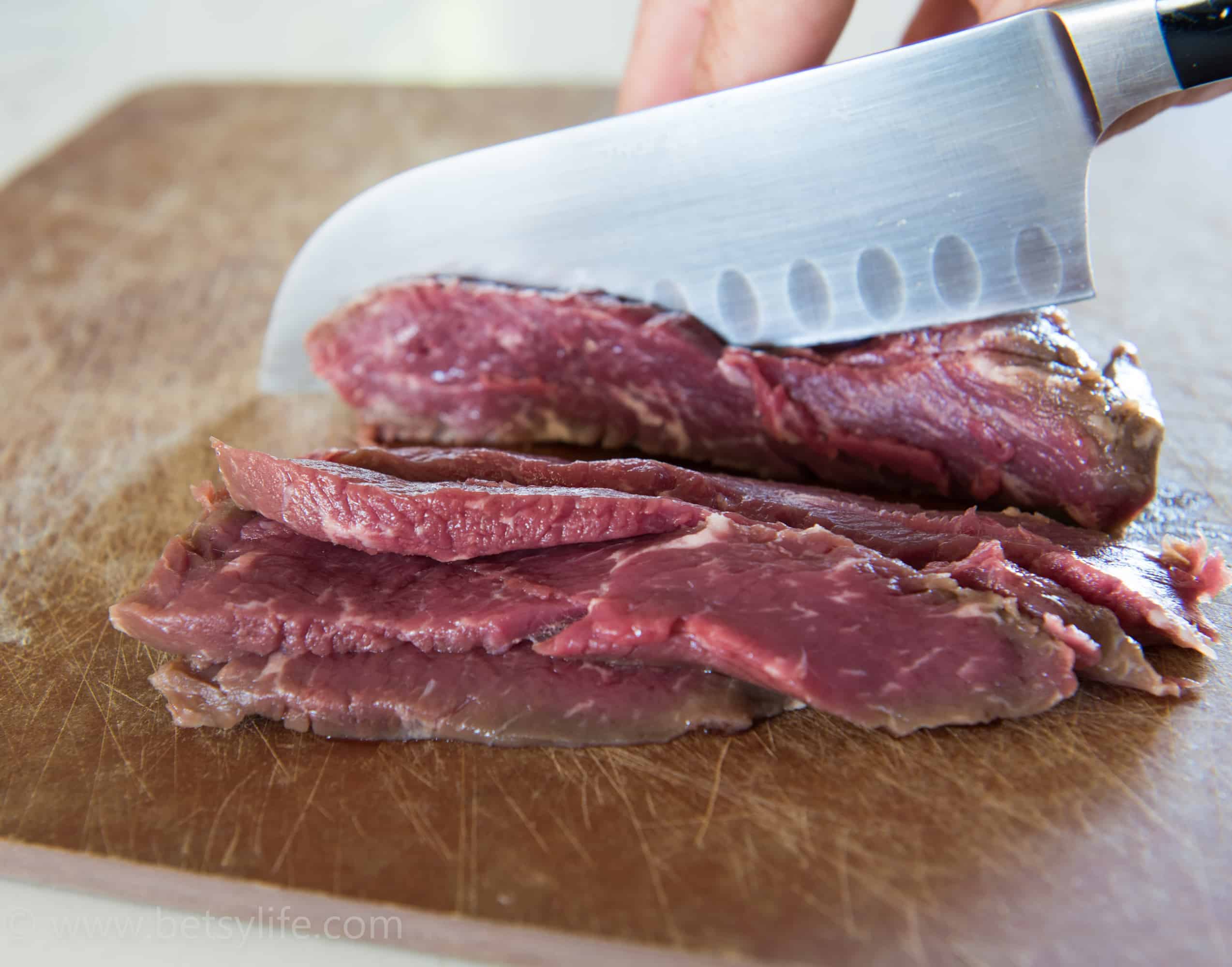 Steak being thinly sliced on a wooden cutting board 
