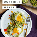 Two Spiralized zucchini nests on a white plate with runny yolk eggs on top. Fork to the right and a purple napkin underneath