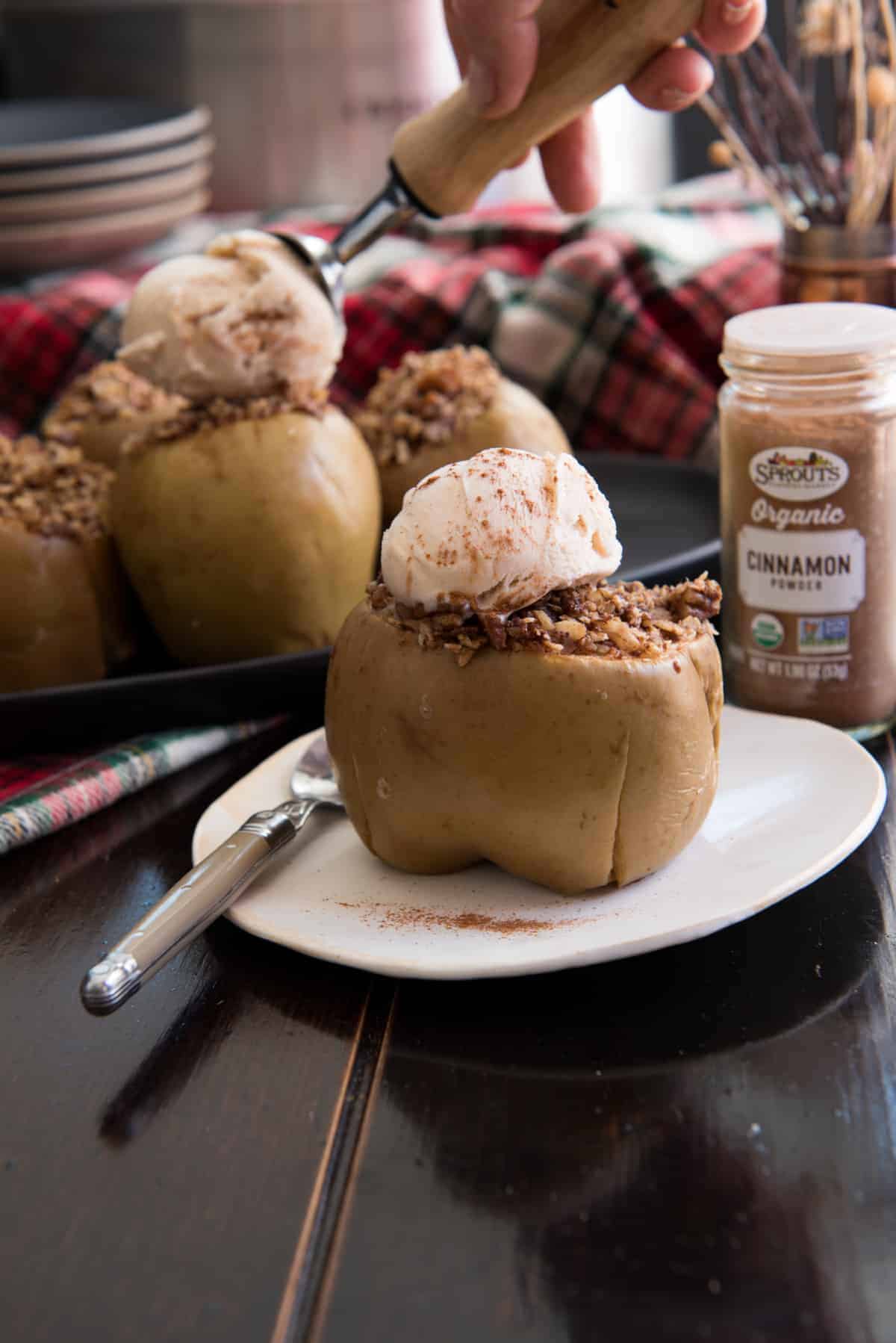 Baked apple stuffed with oatmeal topped with melting ice cream on a white plate with a spoon