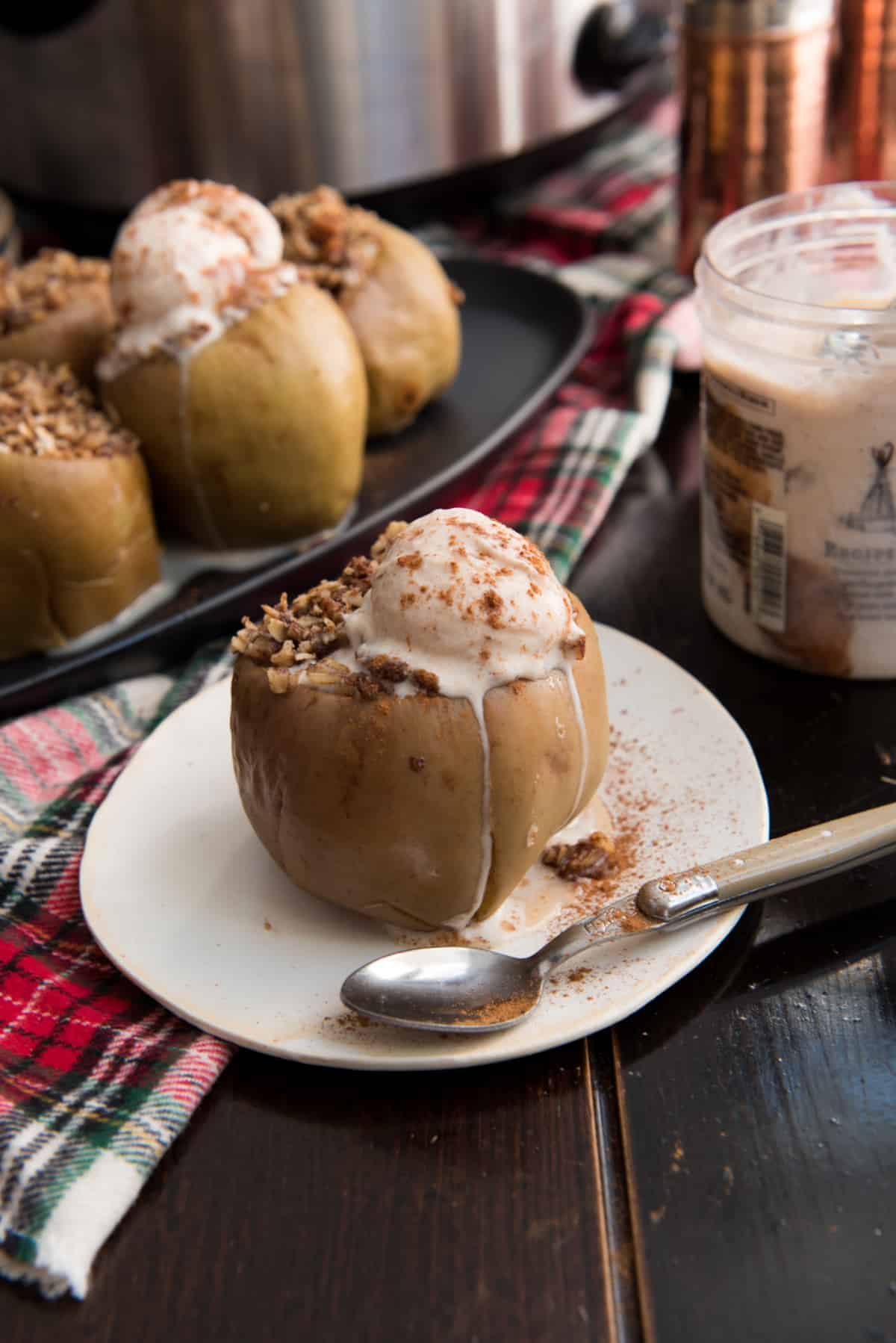 baked apple stuffed with oats on a white plate with melting ice cream and cinnamon sprinkles 