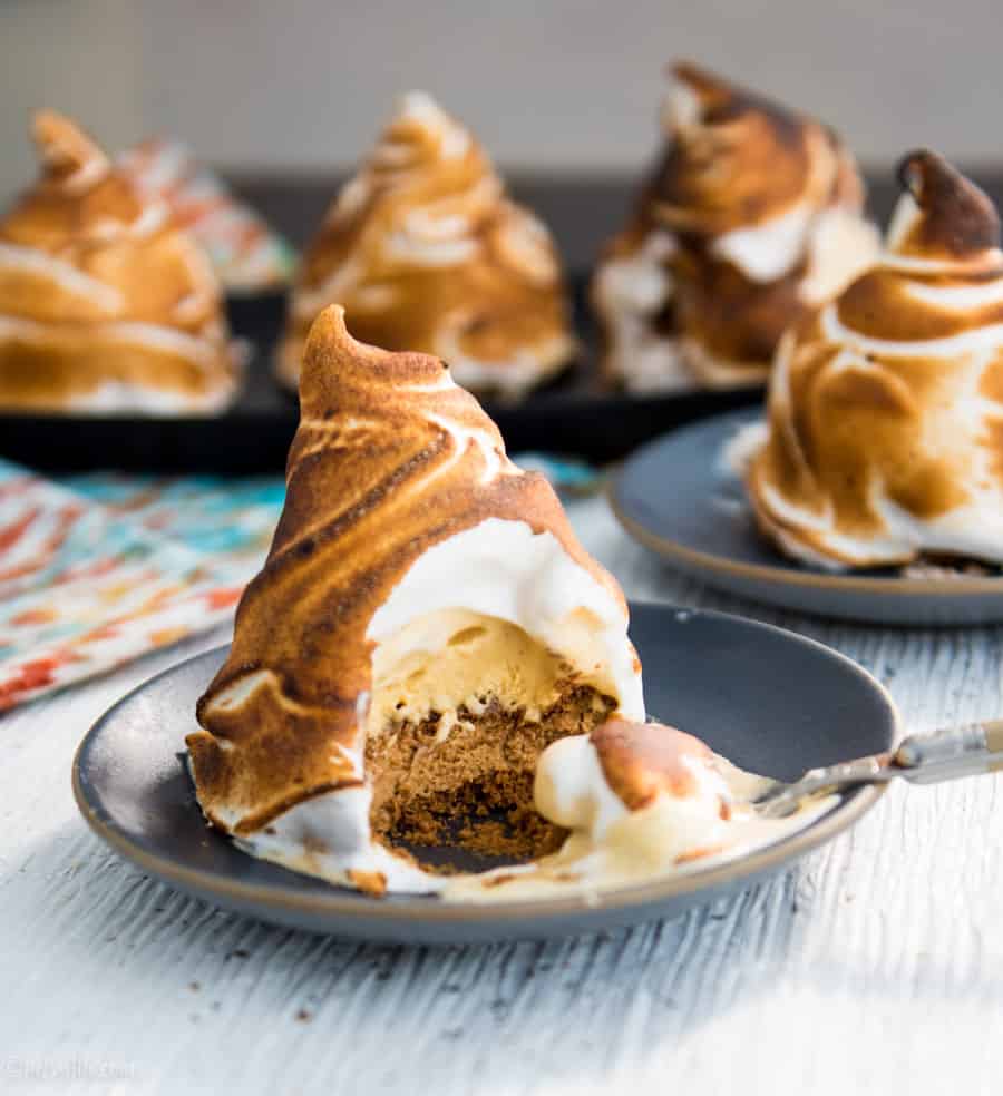 5 individual baked alaska on plates. One in front has a scoop taken out of it to expose a layered interior