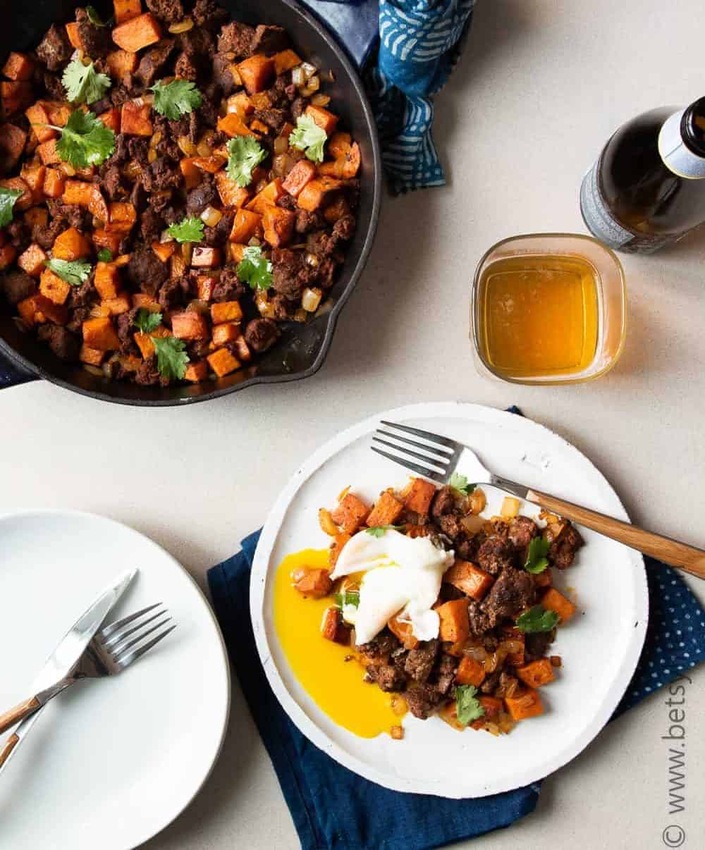 skillet of sweet potato and chorizo hash next to a plated serving topped with a poached egg