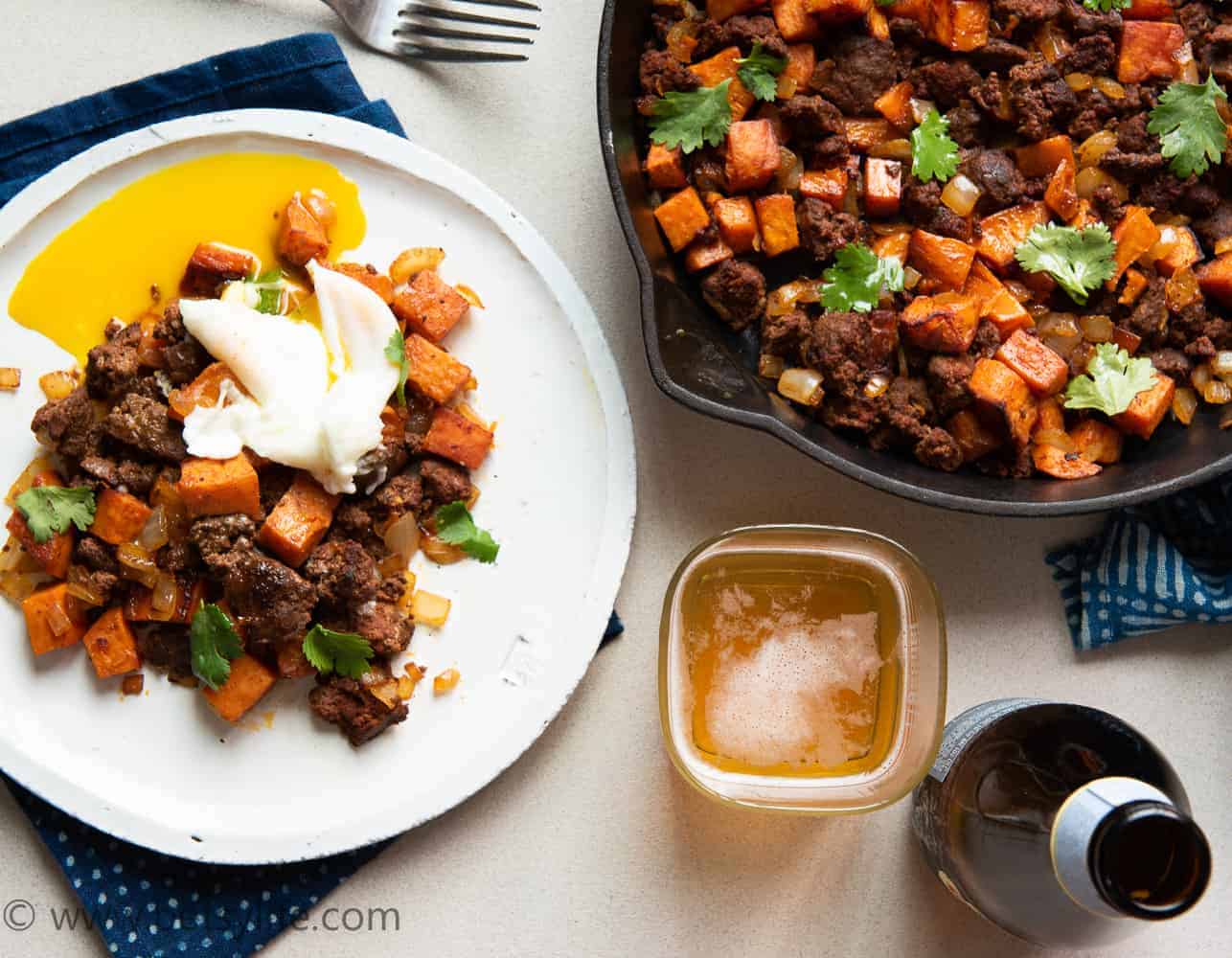 skillet of sweet potato and chorizo hash next to a plated serving topped with a poached egg
