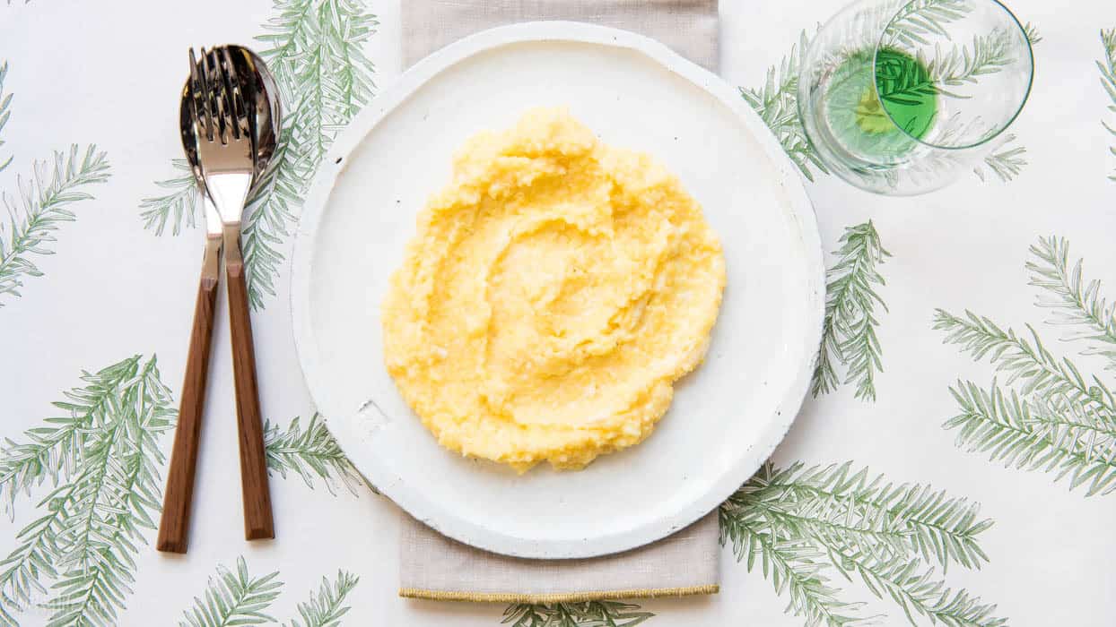 white plate with creamy polenta spread in a circle on a pine bough printed placemat 