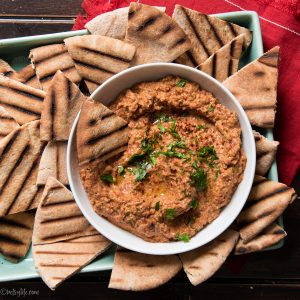 bowl of muhammara roasted red pepper and walnut dip on a platter of grilled pita bread cut into triangles