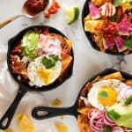three small skillets filled with chilaquiles rojas and topped with different toppings