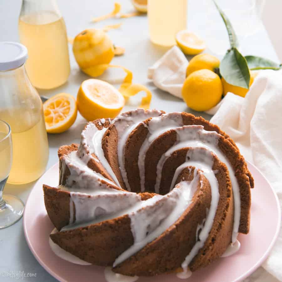 homemade limoncello bundt cake on a pink plate surrounded by bottles of limoncello and lemon peels
