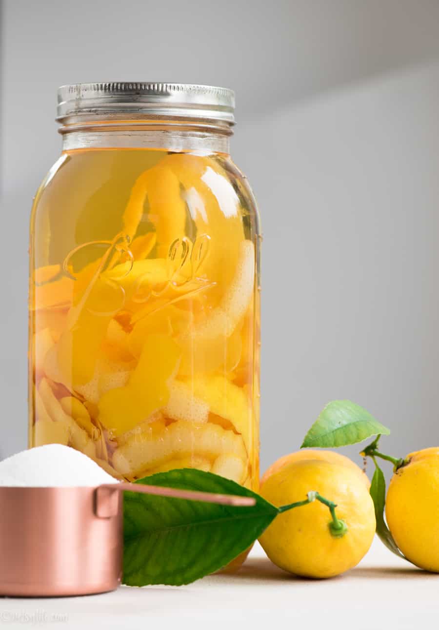 Homemade limoncello. Lemon peels and vodka in a large jar next to a cup of sugar and fresh lemons 