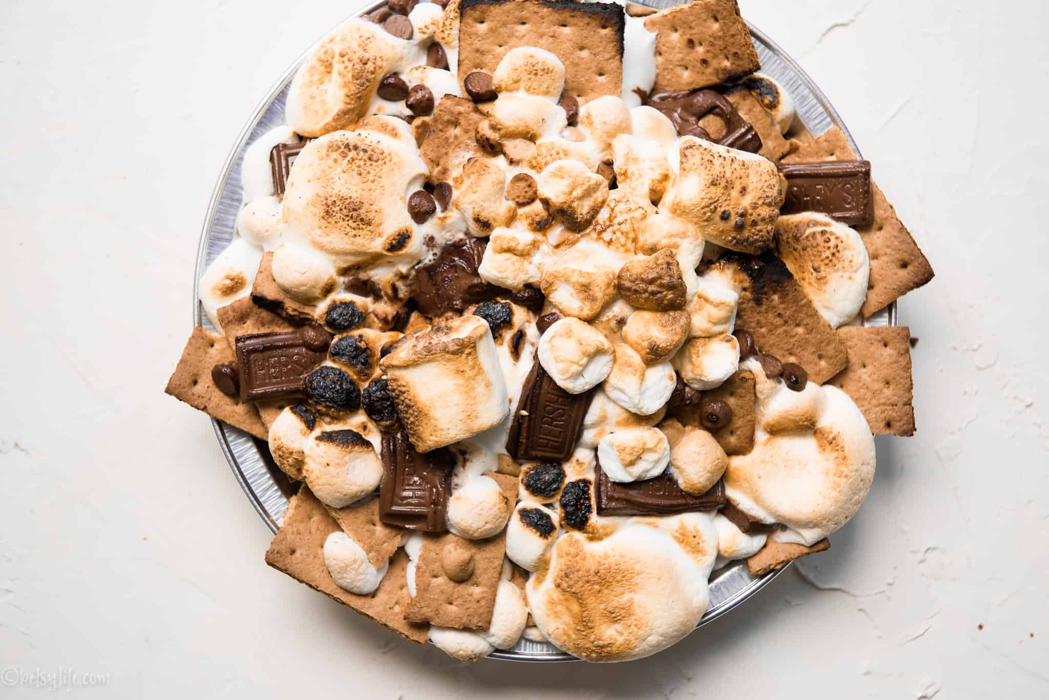 round metal pie pan with golden brown marshmallows, chocolate and graham crackers