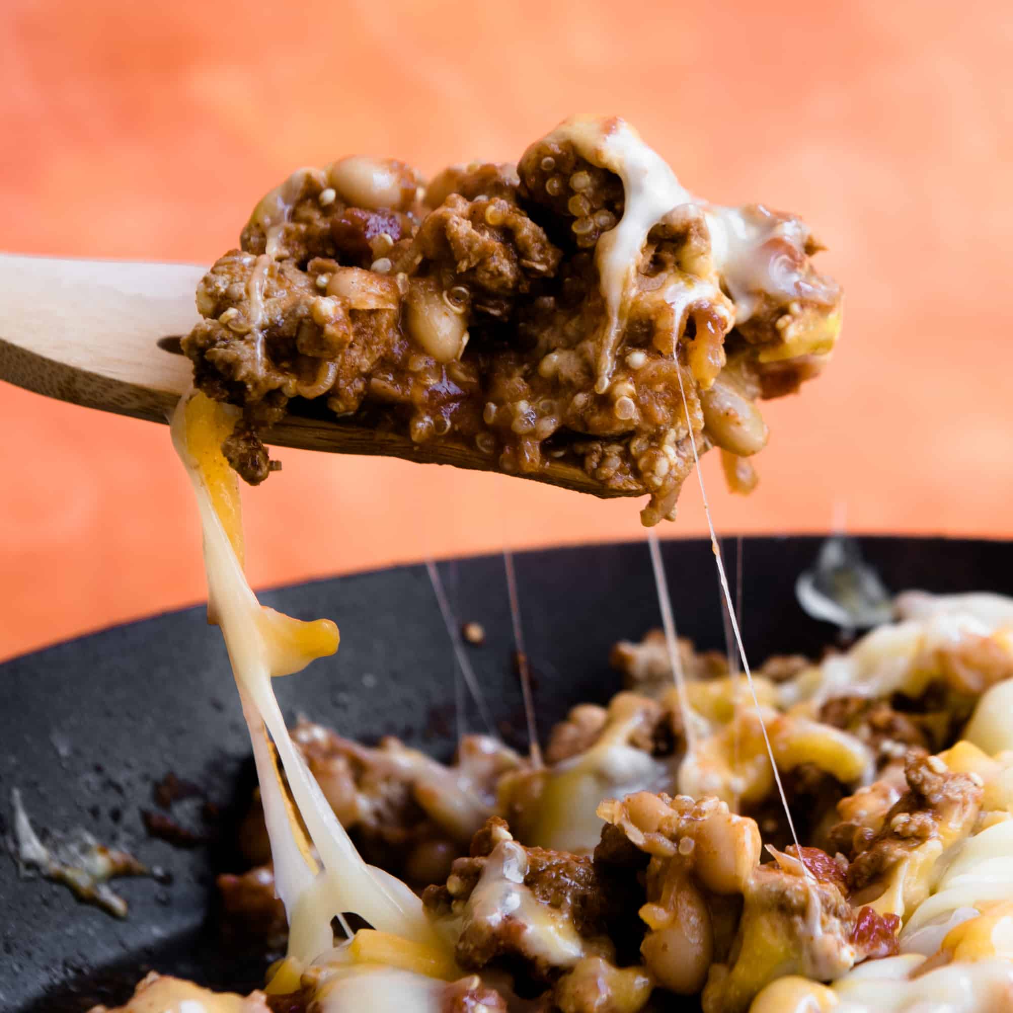 wooden spoon pulling a cheesy serving of taco casserole from a skillet