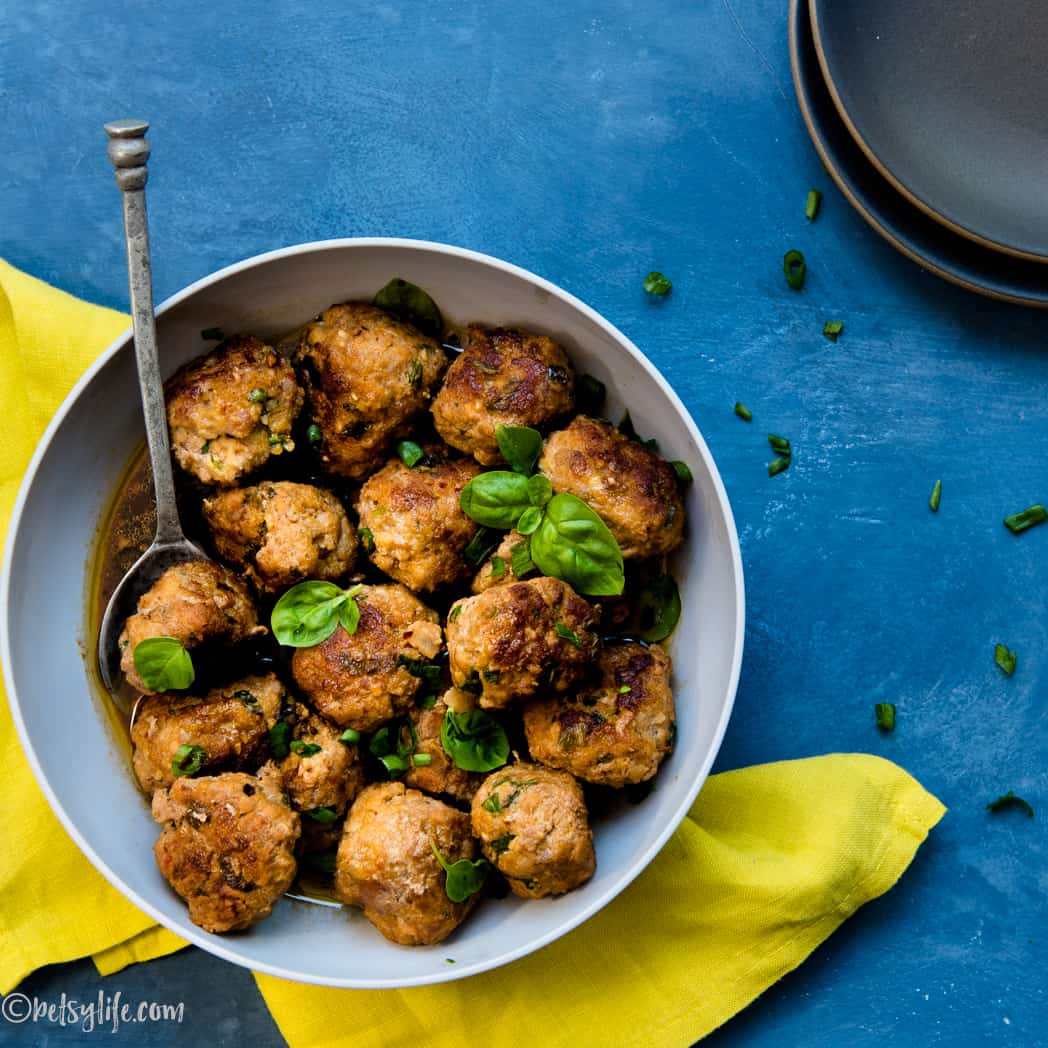 bowl of asian pork meatballs with a metal spoon on a blue surface with a yellow napkin