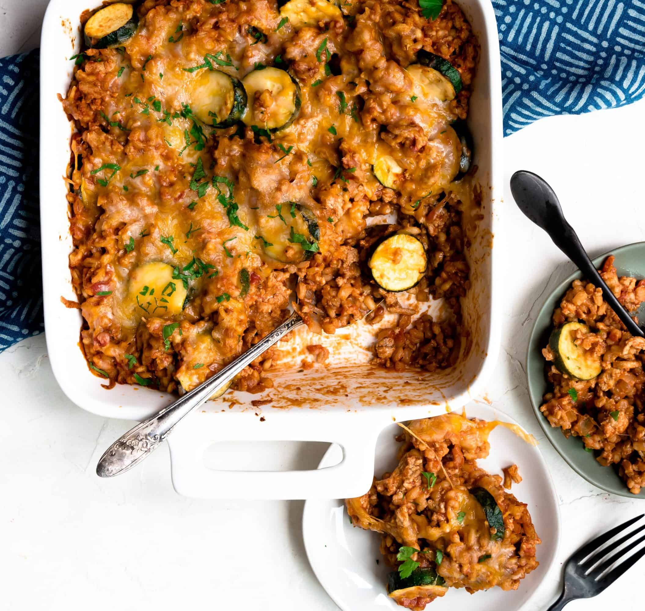 Make Ahead Cheesy Zucchini and Turkey Casserole in casserole dish with two serving plates