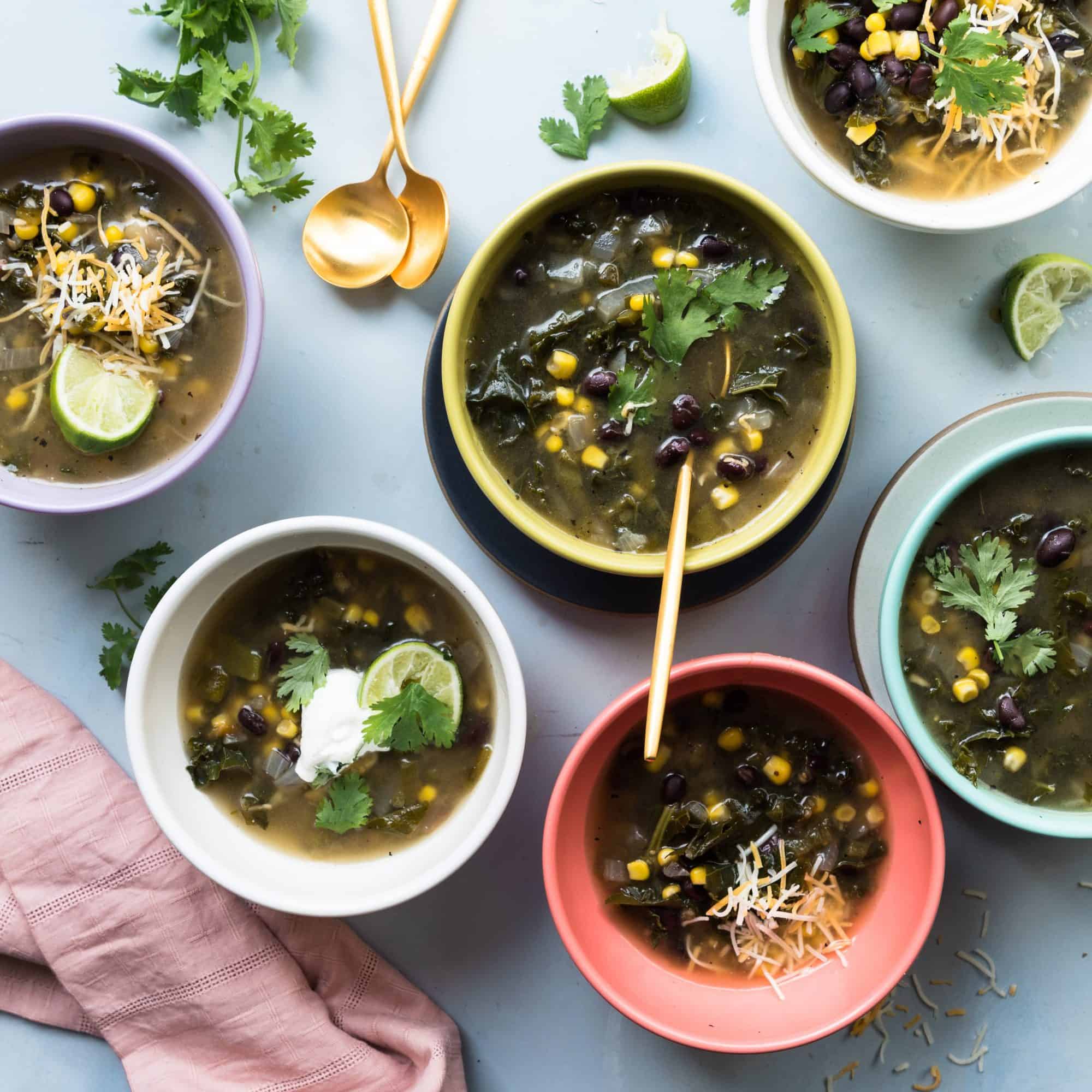 multicolored bowls filled with black bean and kale soup with gold spoons and a pink napkin 