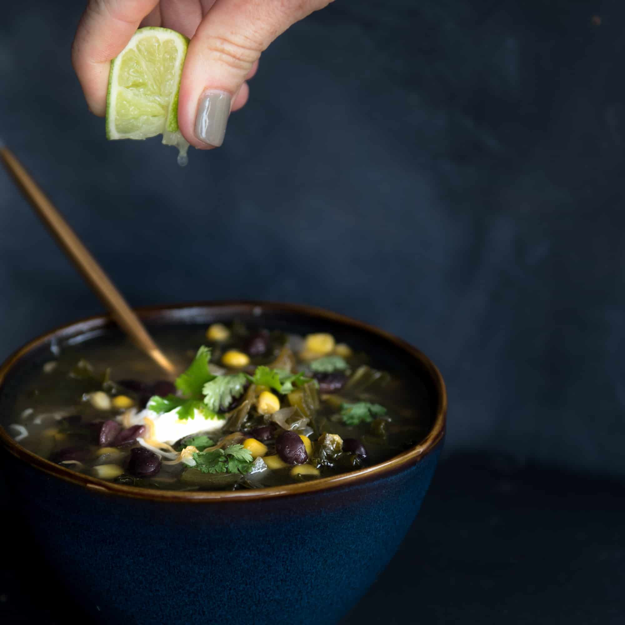 hand squeezing a lime over a bowl of black bean soup
