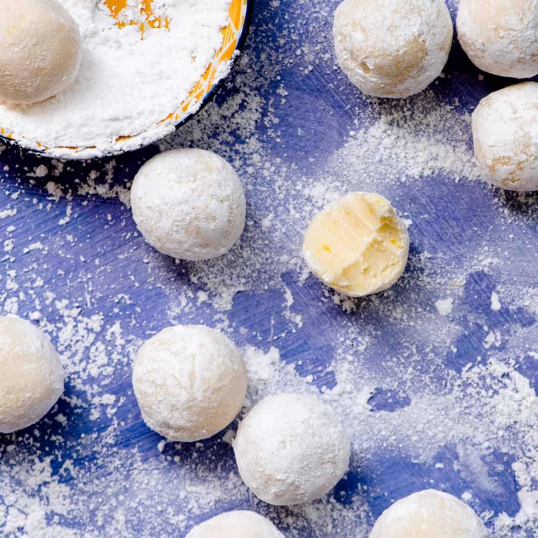 Detail of white chocolate lemon truffles covered in powdered sugar. One truffle has a bite taken out of it