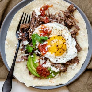 tortilla topped with shredded beef, eggs, avocado, salsa and cilantro with a fork